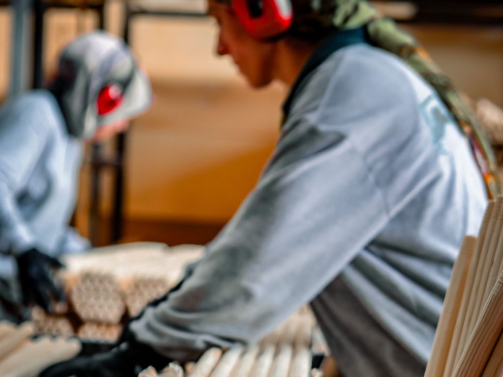 Due operai con cuffie antirumore lavorano manici di legno su una linea di produzione