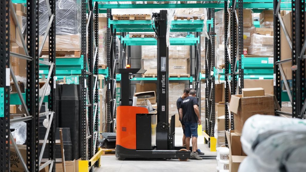 Un addetto manovra un transpallet elettrico in una corsia di magazzino fra scaffalature cariche